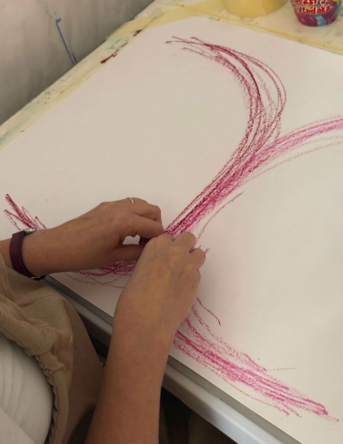 Klientka kreslí oběma rukama symetrický tah magenta pastelkou