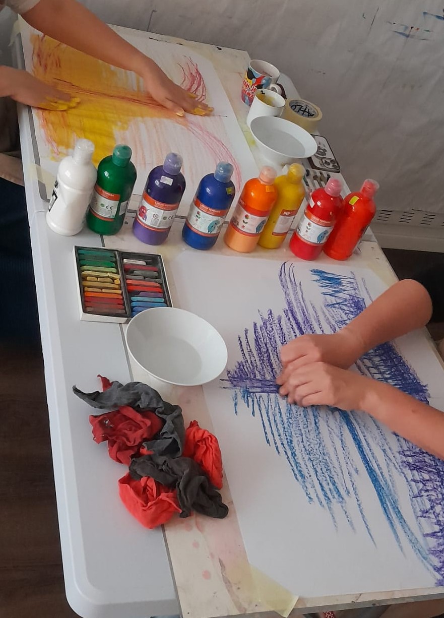 Stůl s pastelkami, prstovými barvami a rozpracovanými kresbami